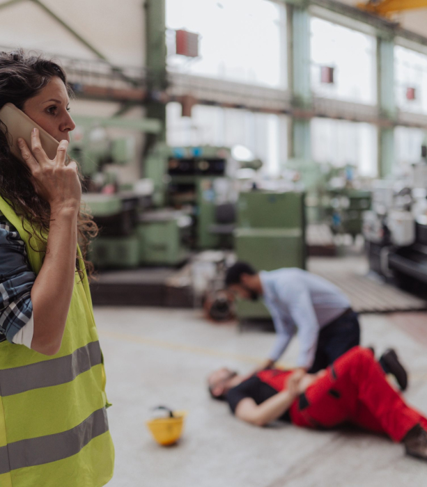 A woman is calling ambulance for her colleague after accident in factory. First aid support on workplace concept.